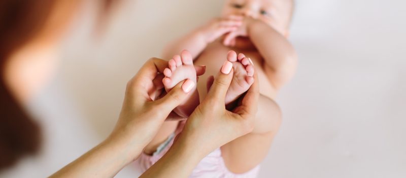 Mother hand massaging foot of her baby on white background