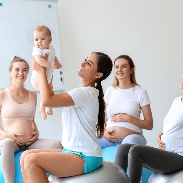 Female coach with baby and pregnant women training in gym